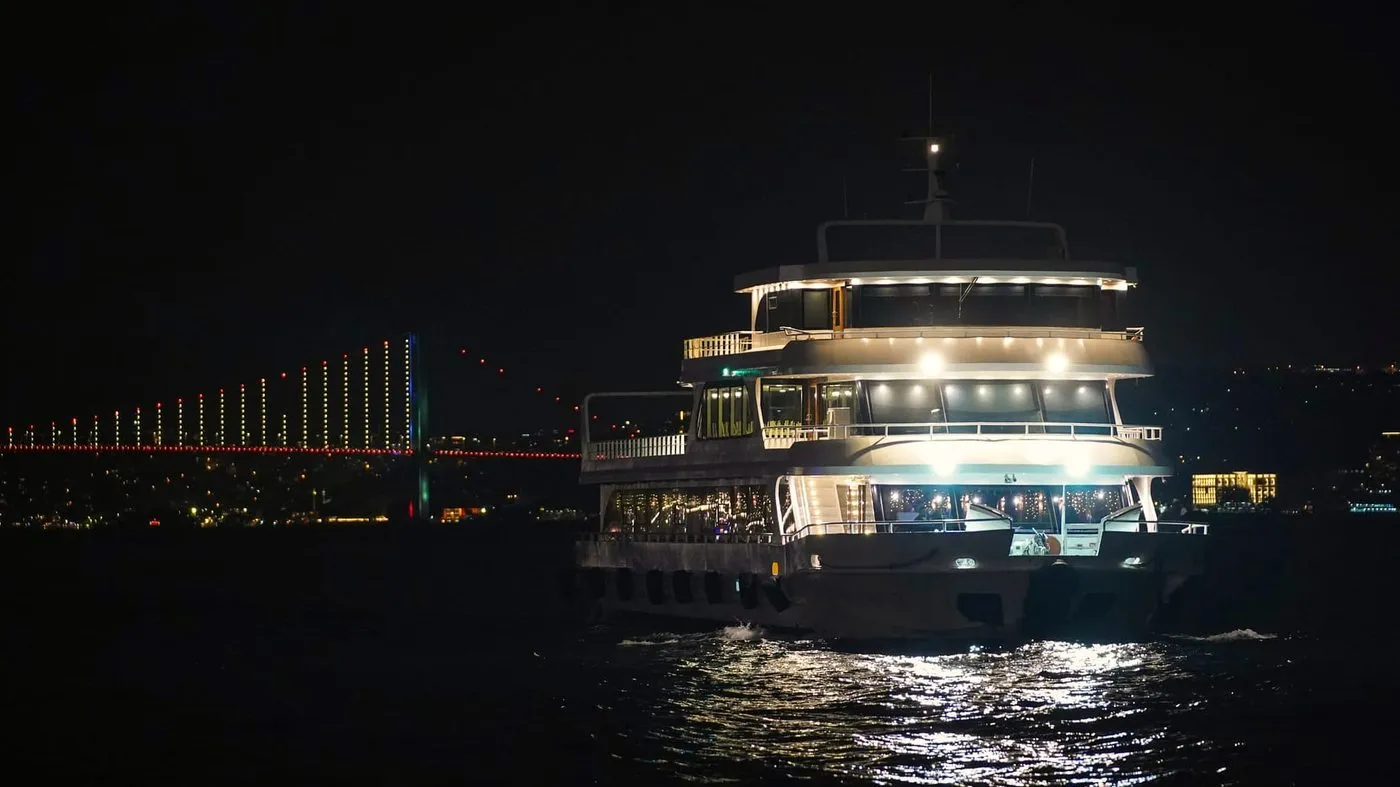The dinner cruise boat lit up at night with the bridge behind
