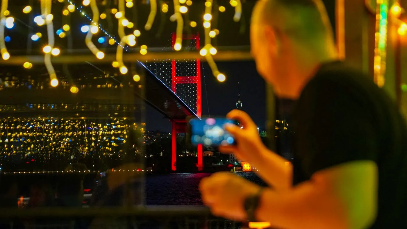 A guest photographing the lit Bosphorus Bridge through the salon window