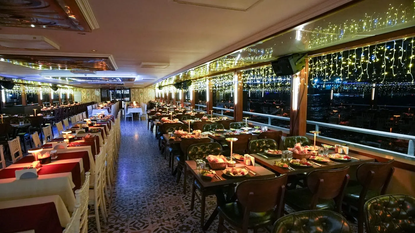 The dining salon at night with laid tables, table lamps and string lights along the windows