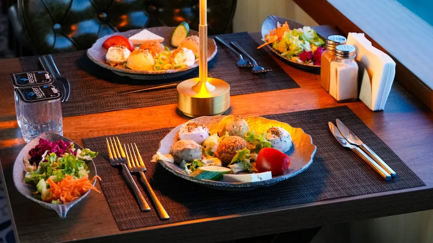 Plates of cold mezes and salad on a table lit by a gold lamp