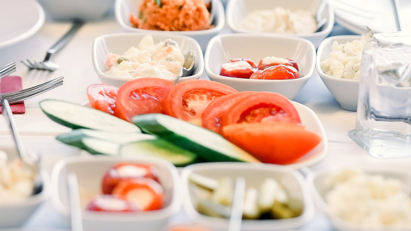 Cold Turkish mezes in small white bowls around a plate of sliced tomato and cucumber