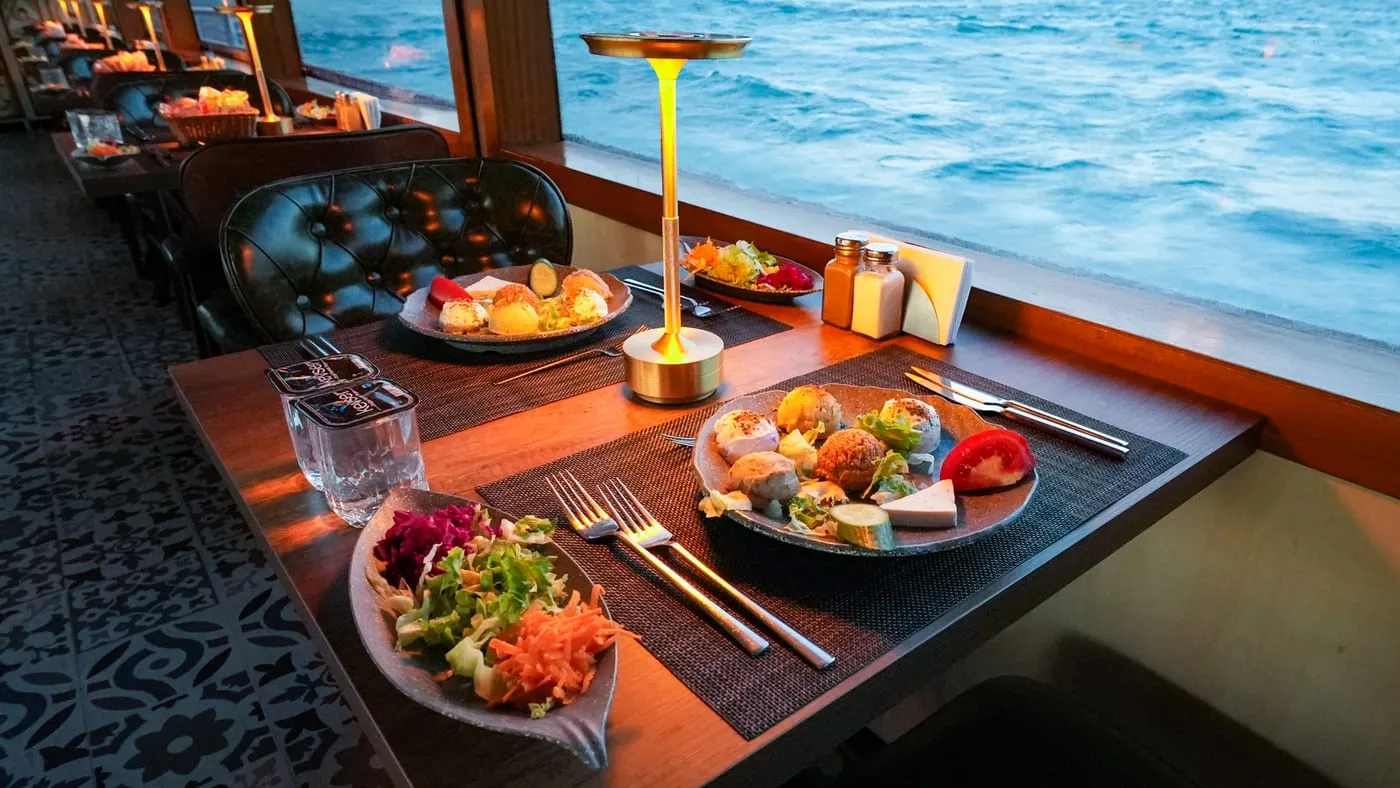 Window tables laid with mezes and salads, lamps glowing at dusk