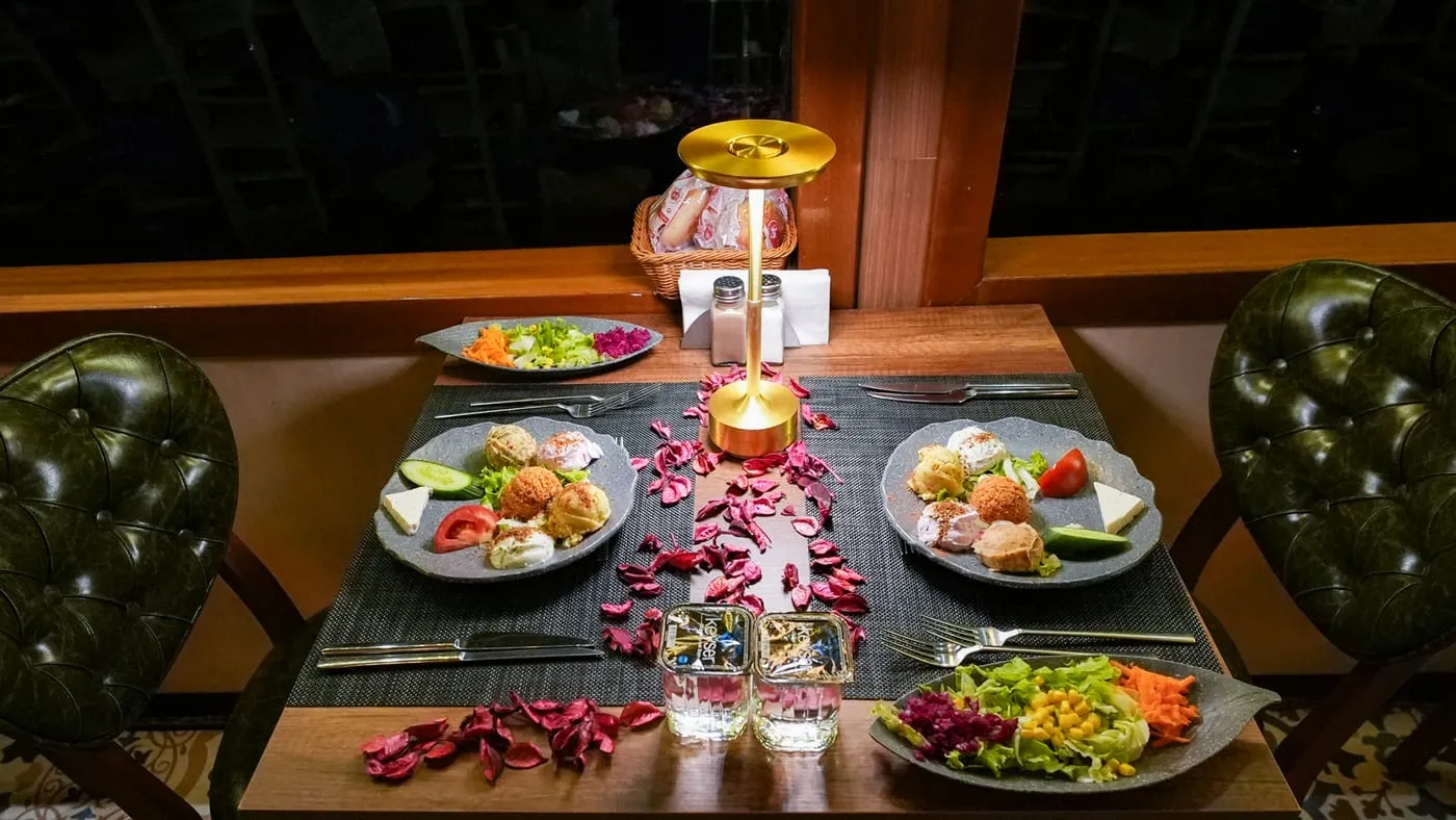 A table for two at the window, set with rose petals and a lamp