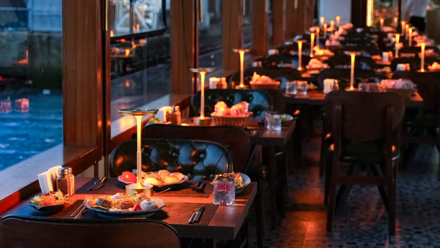 The salon at dusk with a lamp on every table and the water outside