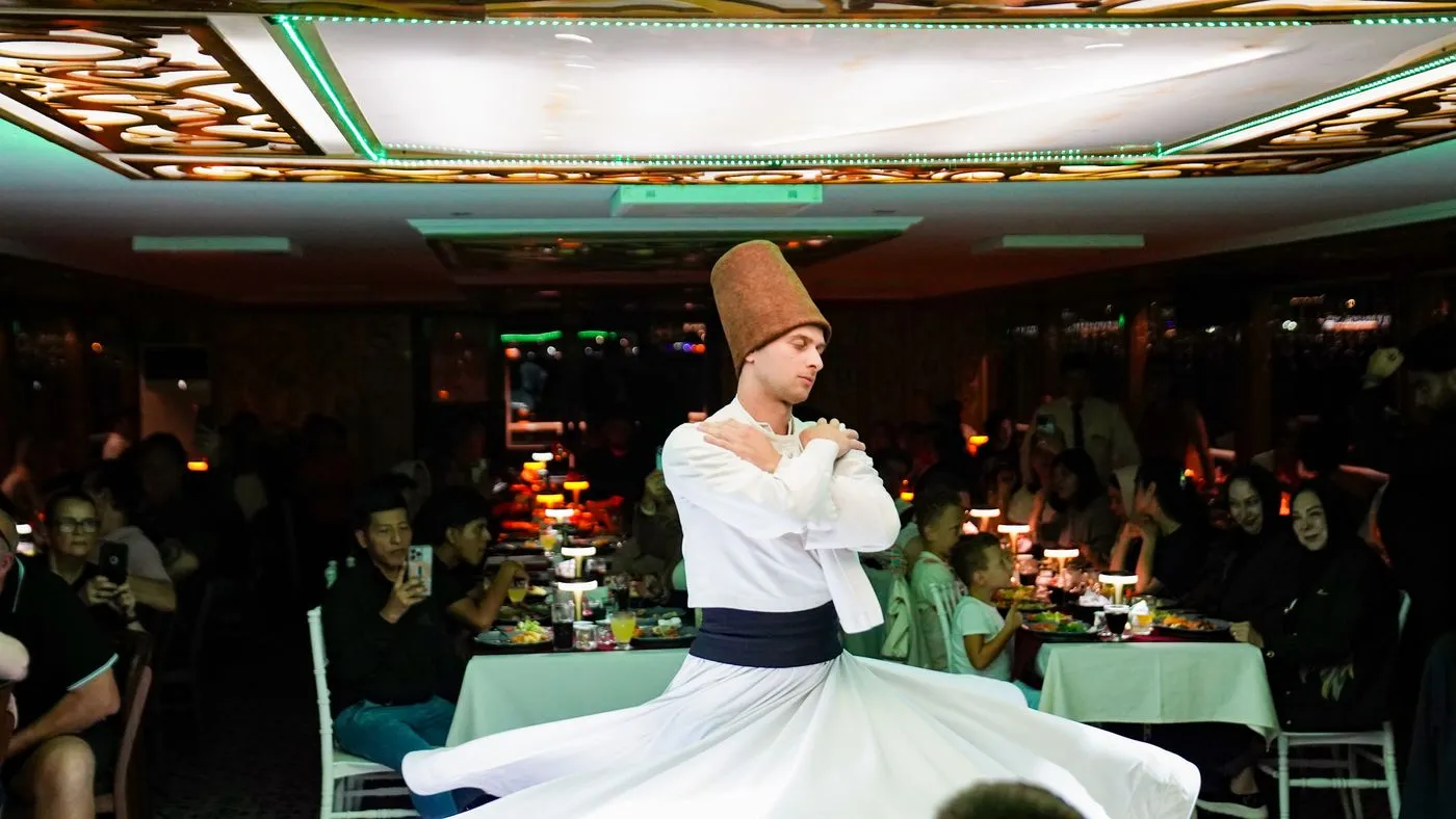 A whirling dervish turning between the tables in the lamplit salon