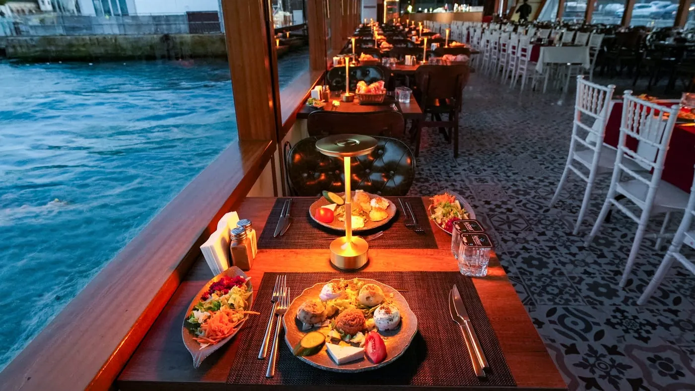Window table laid with mezes at dusk, the water just outside the glass