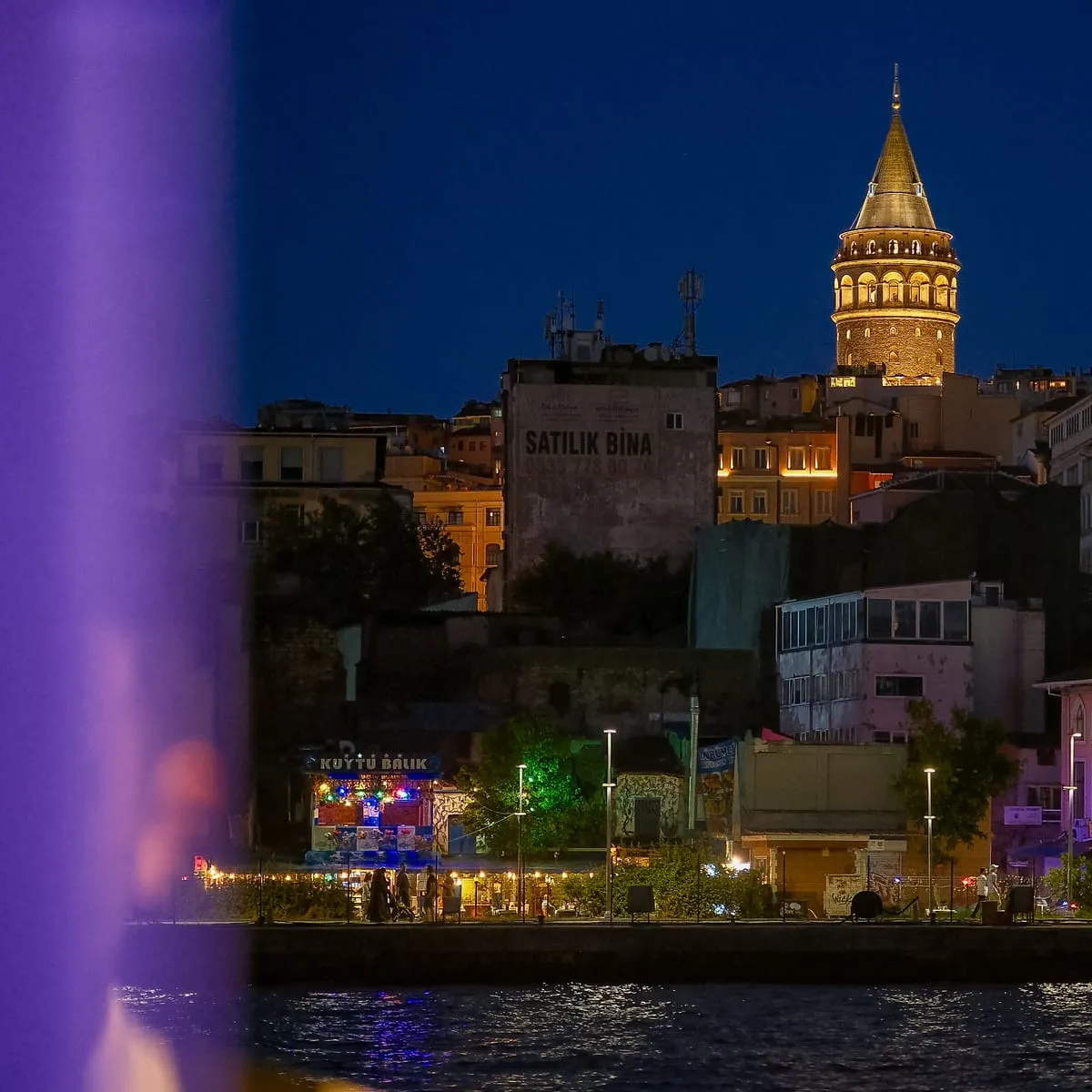 Galata Tower lit up at night above the Golden Horn shore